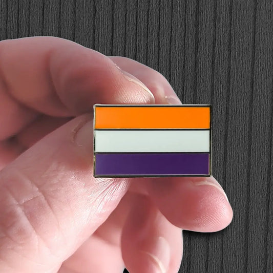 Hand holding a pride flag pin with orange, white, and purple stripes against a dark background