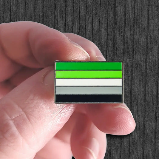 Hand holding a flag pin with green, white, and black stripes against a dark background
