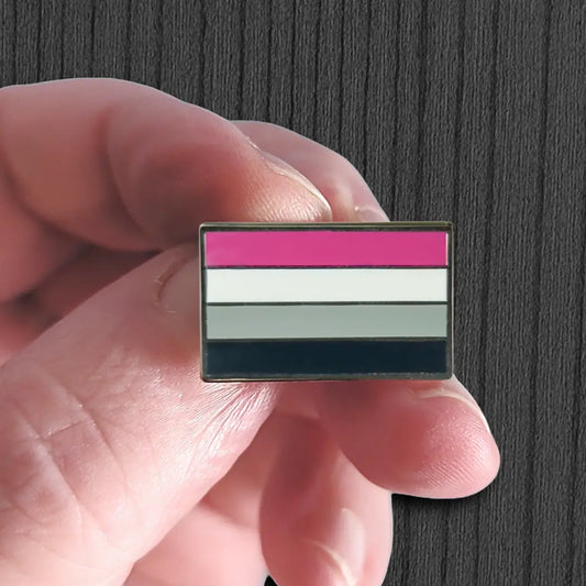 Hand holding a small flag with purple, white, gray, and black stripes against a dark background