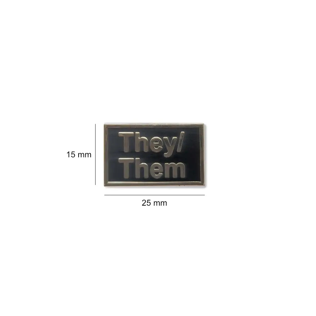 Small They/Them enamel lapel pin measuring 25 millimeters wide by 15 millimeters tall, featuring silver text on a black background to proudly display gender-neutral pronouns.