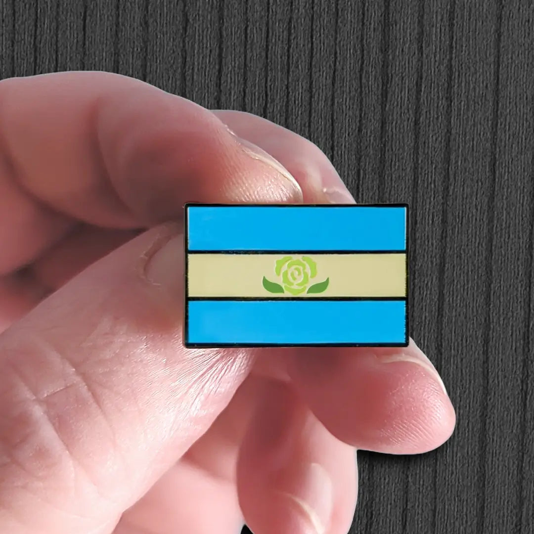 Small flag pin with a blue and beige design held between fingers against a dark background