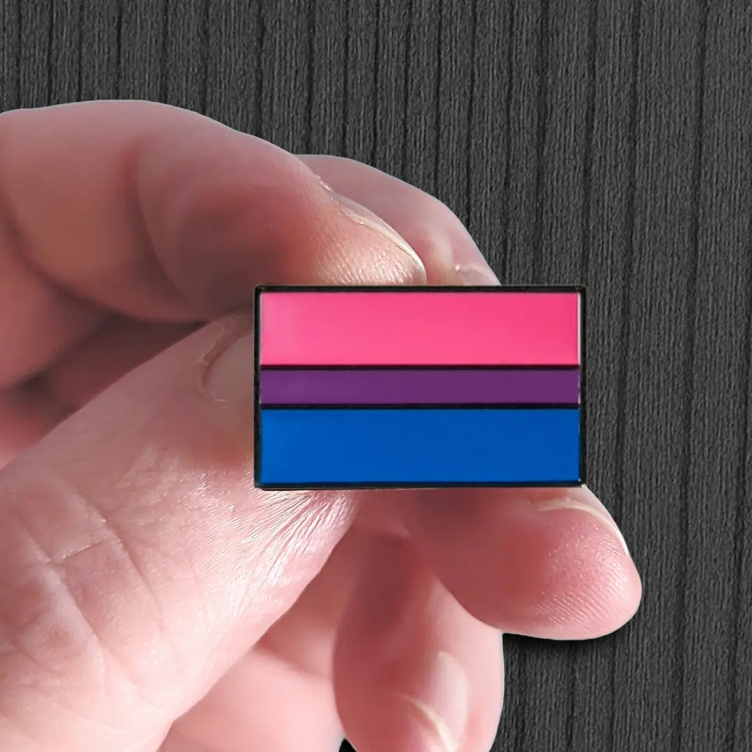 Hand holding a bisexual pride flag pin against a dark background