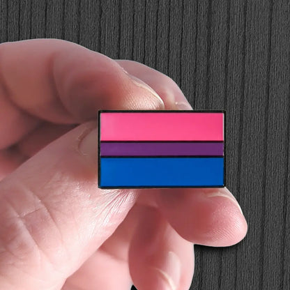 Hand holding a bisexual pride flag pin against a dark background