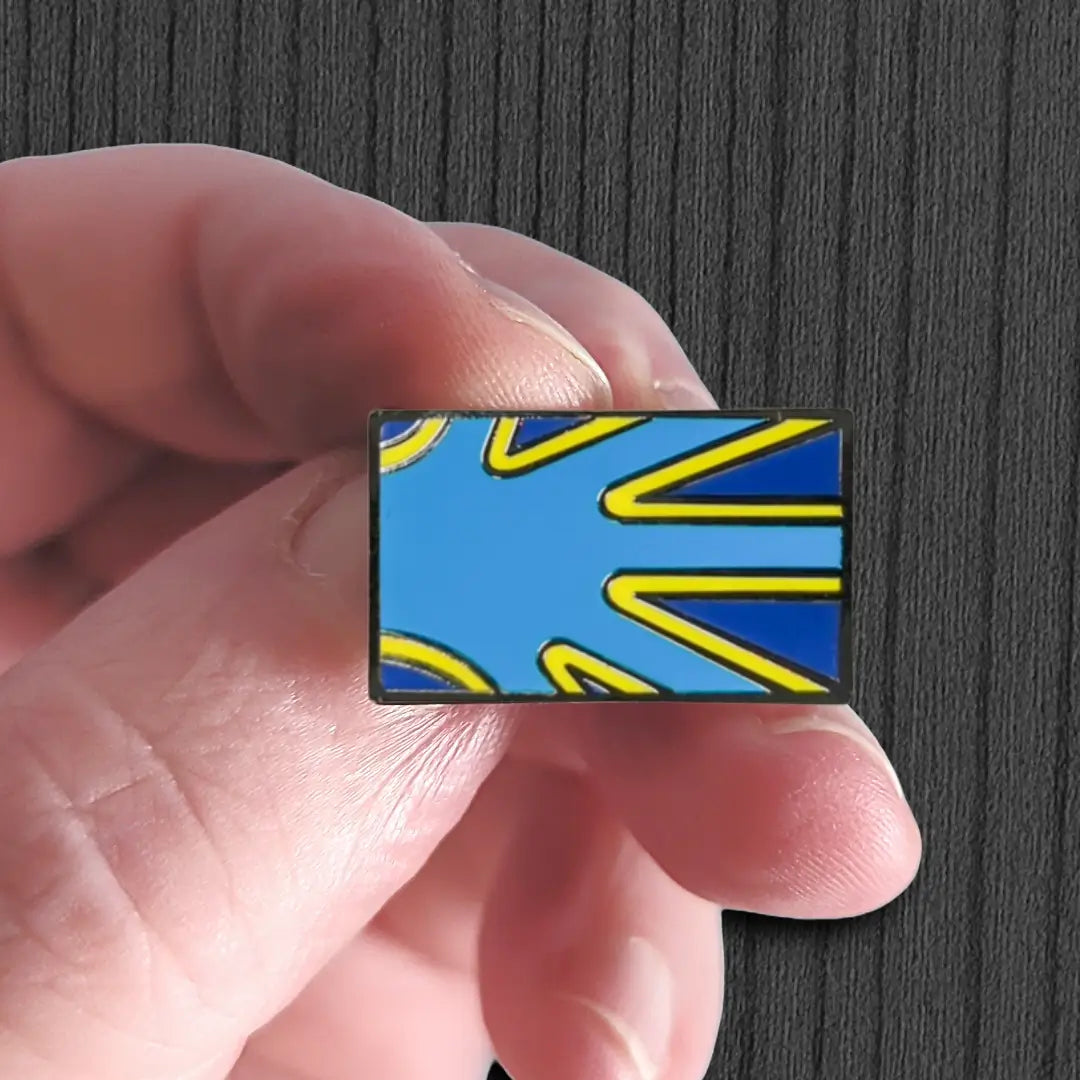 Rectangular blue and yellow enamel pin held between fingers against a dark background