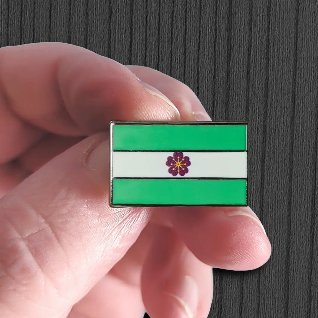 Hand holding a rectangular flag pin with green, white, and purple design on a dark background