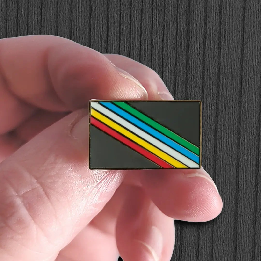 Hand holding a rectangular pin with horizontal stripes against a dark background