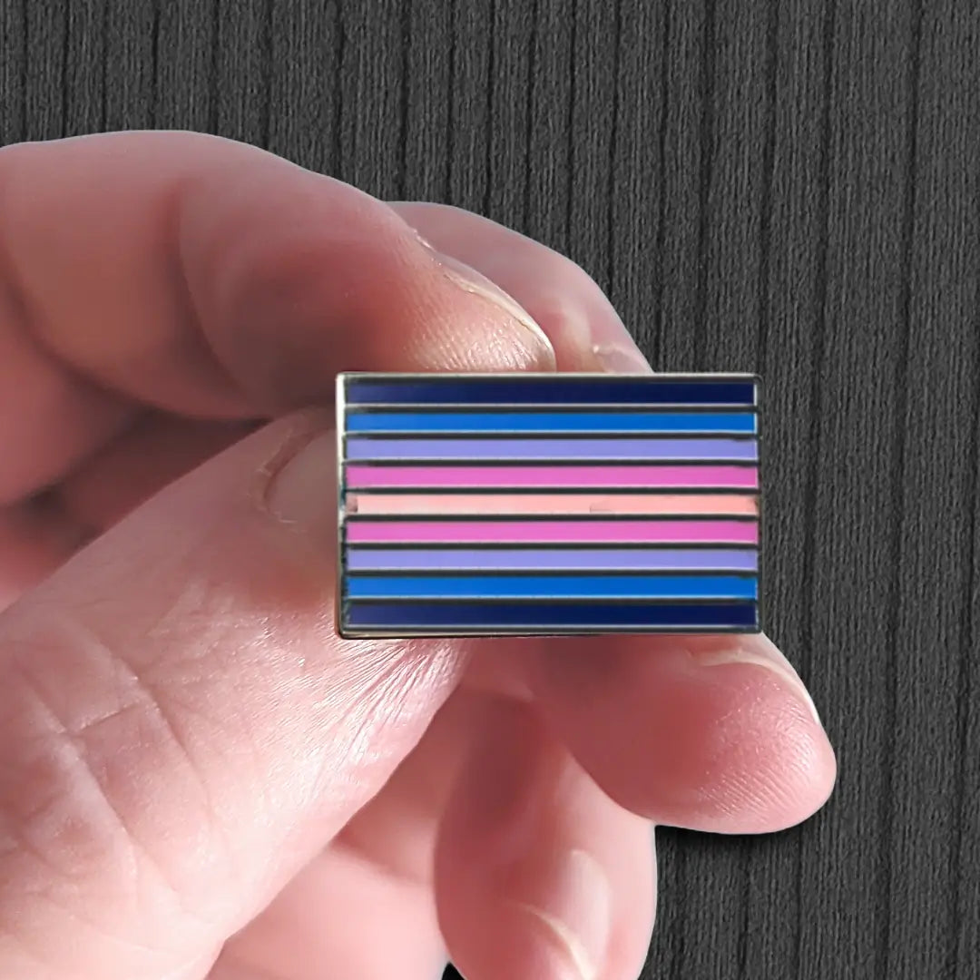 Hand holding a rectangular pin with horizontal stripes against a dark background