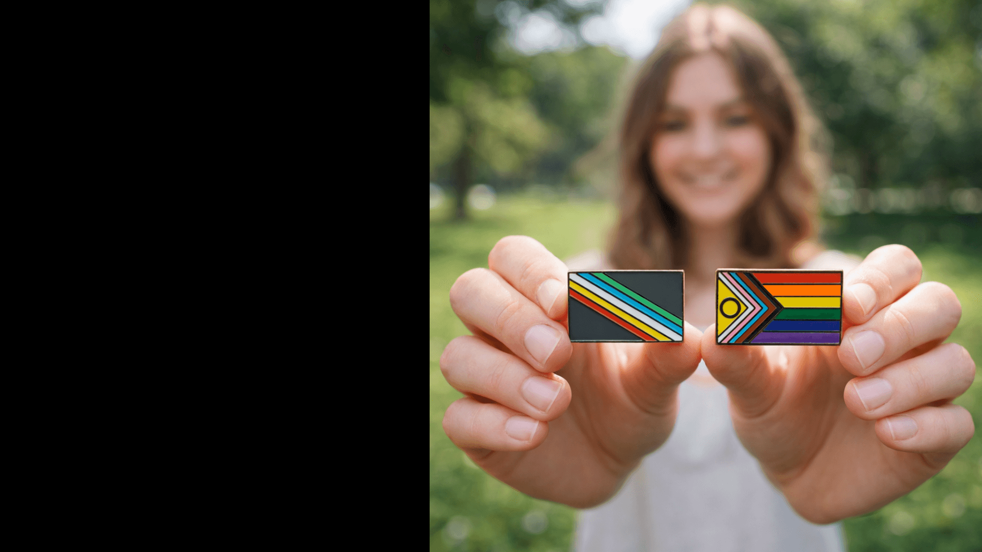 Person holding two small rectangular flags with rainbow designs against a blurred natural background