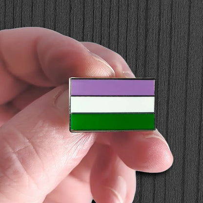 Hand holding a flag pin with purple, white, and green stripes against a dark background