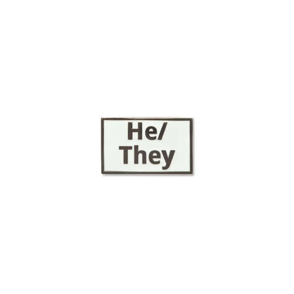 Rectangular He/They lapel pin with a white enamel background and bold black lettering, outlined by a slim metallic border a clear and modern pronoun pin for gender expression.