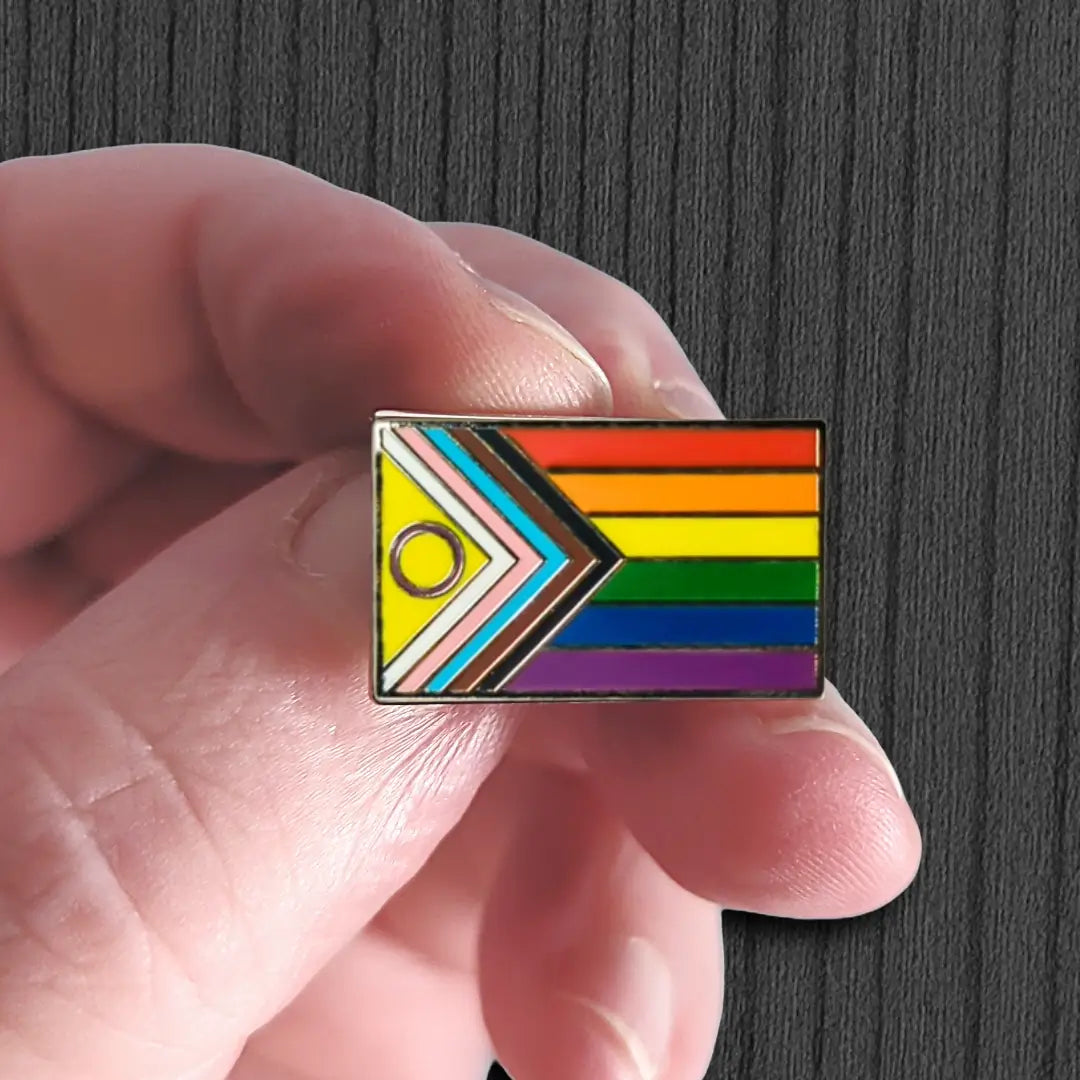 Hand holding a rainbow flag pin with geometric design on a dark background