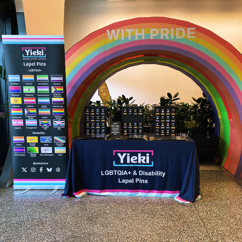 Yieki LGBTQIA+ & Disability Lapel Pins display with rainbow arch and branded tablecloth.