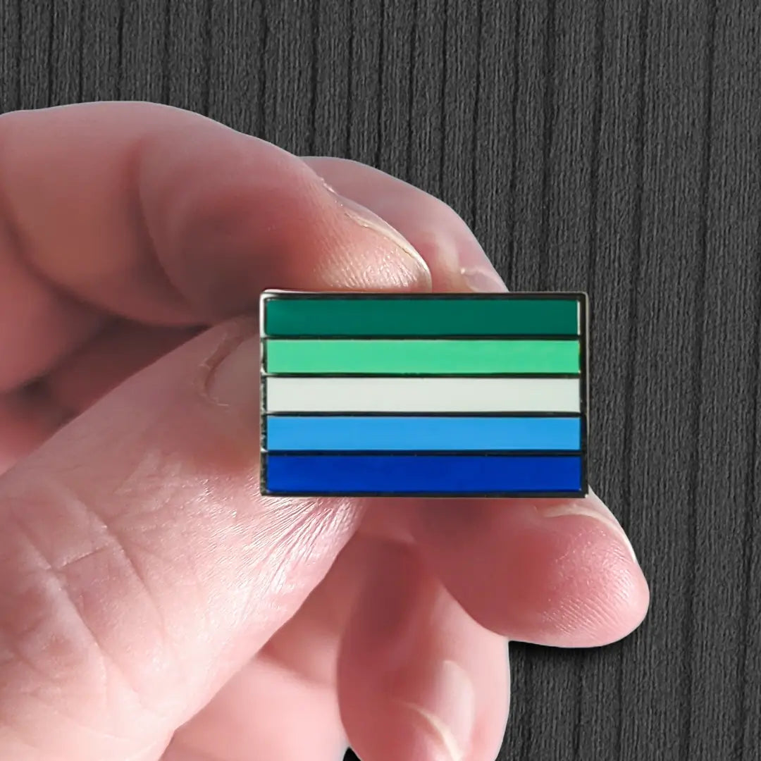 Hand holding a flag-shaped pin with horizontal stripes on a dark background