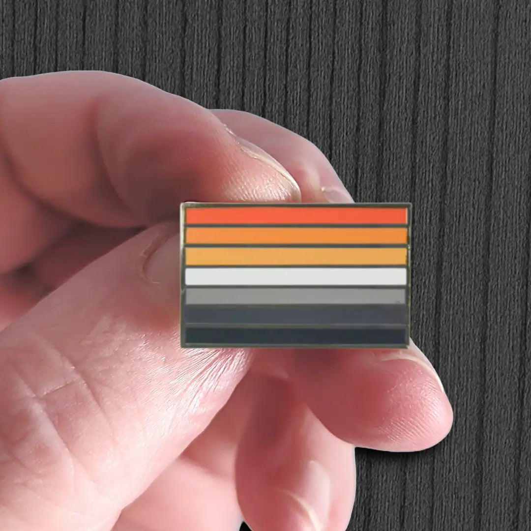 Hand holding a rectangular pin with horizontal stripes against a dark background