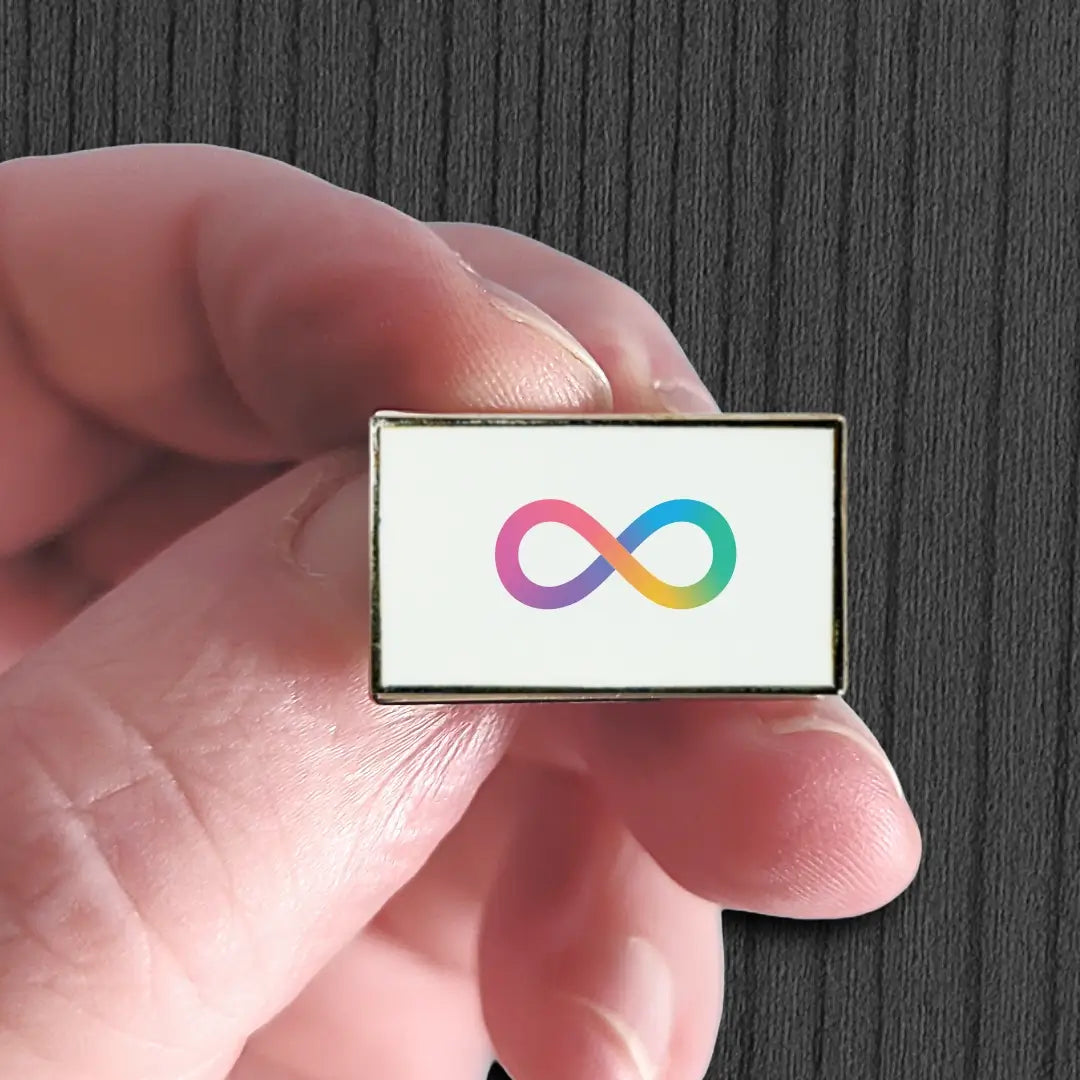 Hand holding a rectangular pin with a colorful infinity symbol on a white background.