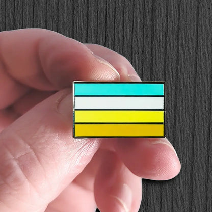Hand holding a rectangular pin with horizontal stripes of blue, white, and yellow against a dark background