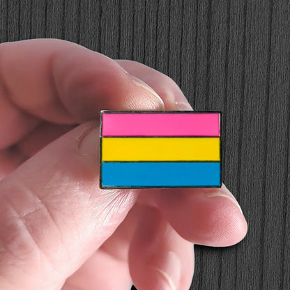 Hand holding a pansexual pride flag pin against a dark background