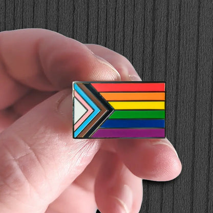 Hand holding a rainbow flag pin against a dark background