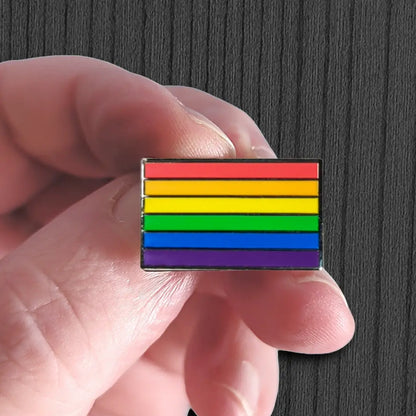 Hand holding a rainbow flag pin against a dark background