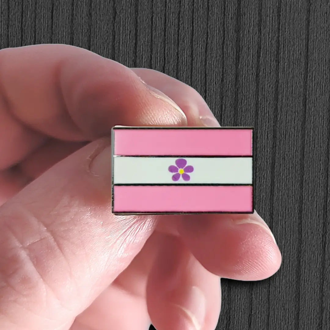 Pink and white striped pin with a purple flower held between fingers against a dark background
