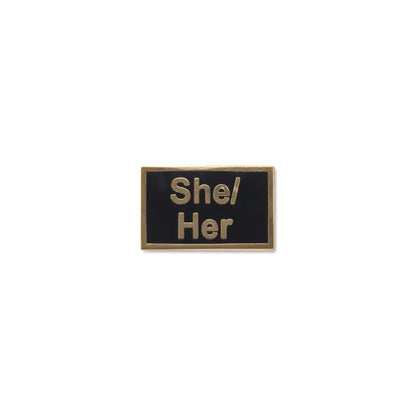Elegant black She/They lapel pin with raised silver-tone lettering and a metallic frame, offering a minimalist and durable pronoun display for daily wear or professional settings.