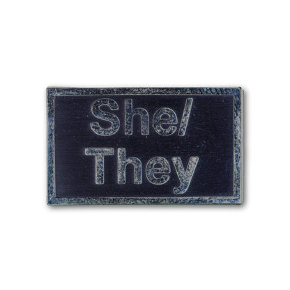 Rectangular patch with 'She/They' text on a black background