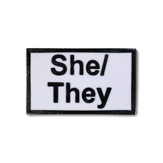 Rectangular enamel pin with 'She/They' text on a white background
