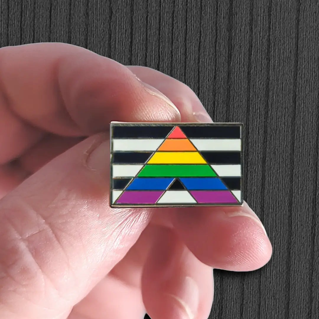 Hand holding a rainbow triangle pin against a dark background