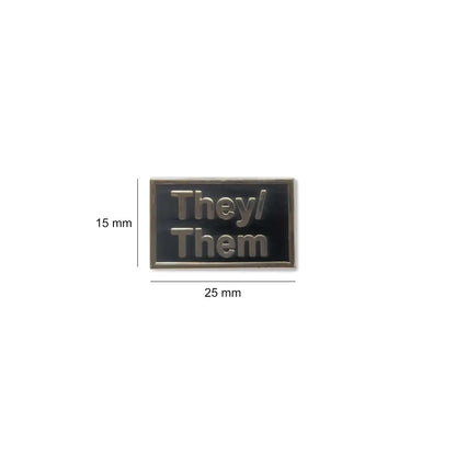 Small They/Them enamel lapel pin measuring 25 millimeters wide by 15 millimeters tall, featuring silver text on a black background to proudly display gender-neutral pronouns.